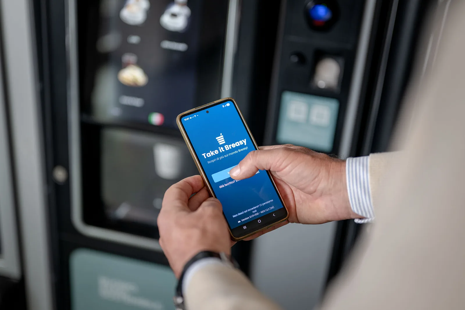 Una persona apre l'app Breasy davanti a un distributore DrinkService