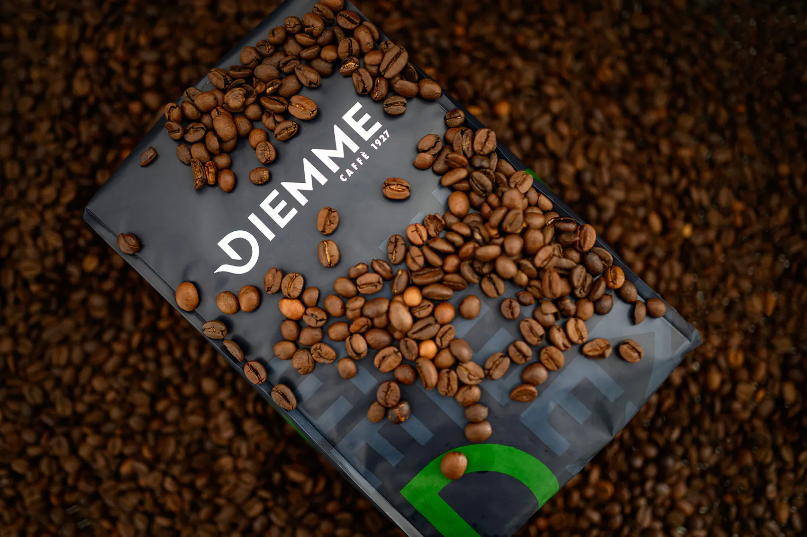 Confezione di caffè in grani Caffè Diemme posata su un letto di chicchi tostati
