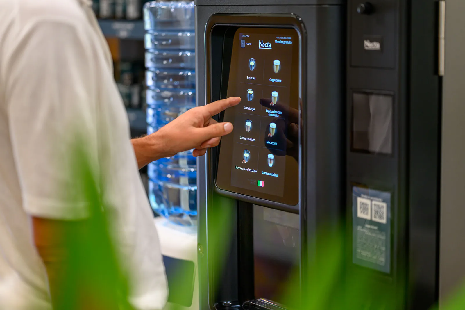 Una persona sceglie una bevanda sul touchscreen del distributore, accanto al boccione pieno.