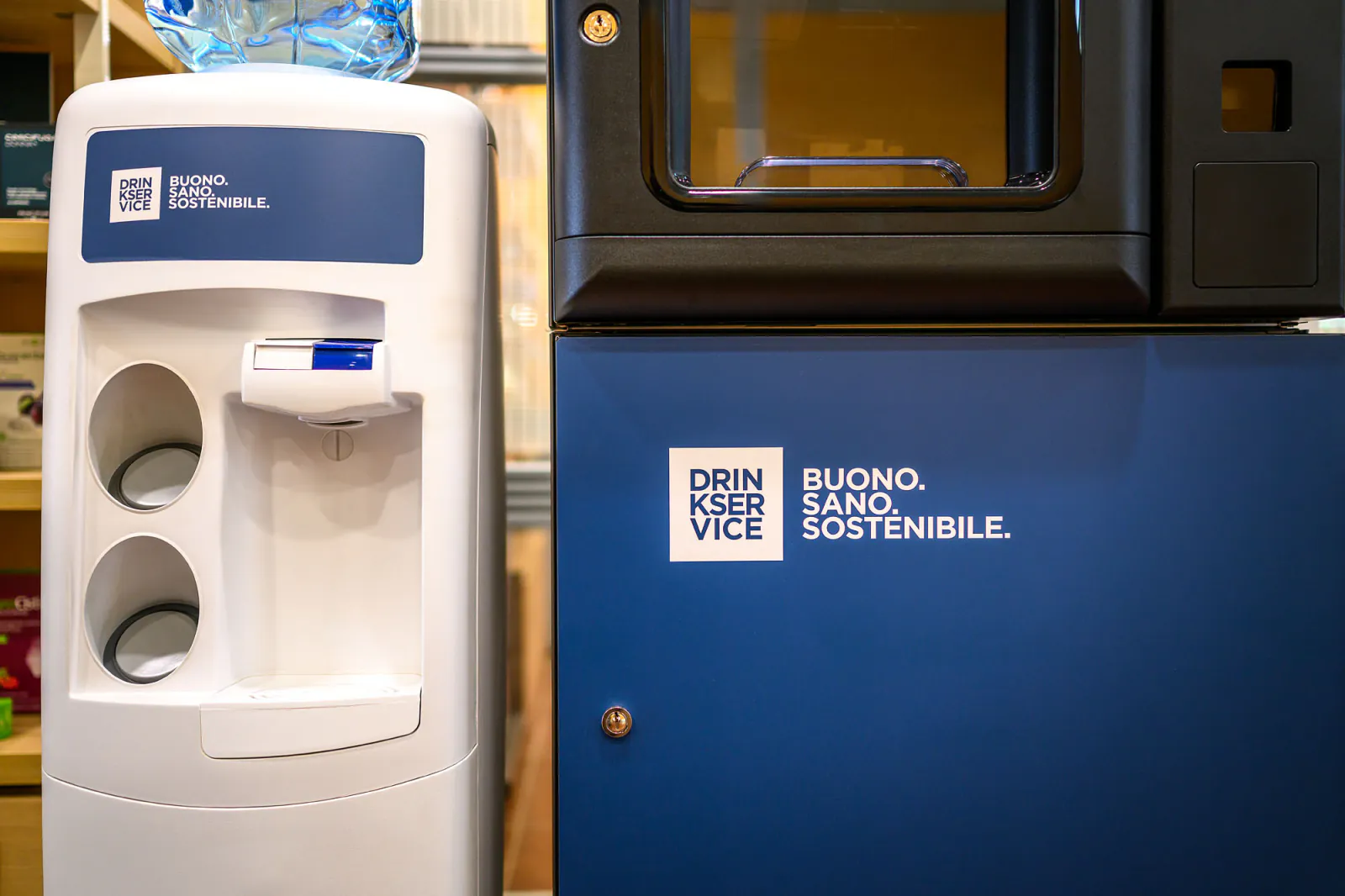 Il dispenser a boccione accanto al fianco blu del distributore, con il payoff "Buono. Sano. Sostenibile." sul pannello.