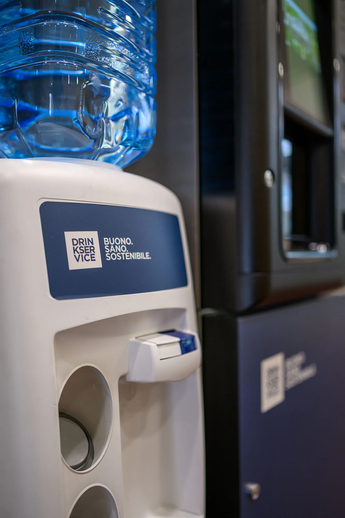 Dettaglio del dispenser con il boccione pieno in cima e l'erogatore a due bocche, accostato al distributore.