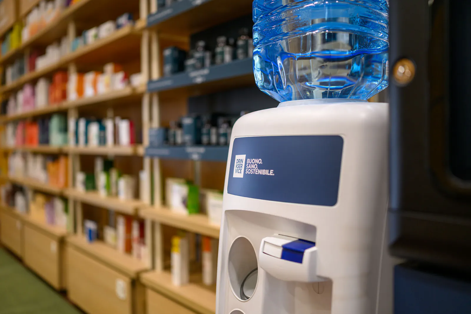Dispenser con boccione d’acqua accanto al distributore, davanti agli scaffali in legno del punto vendita.