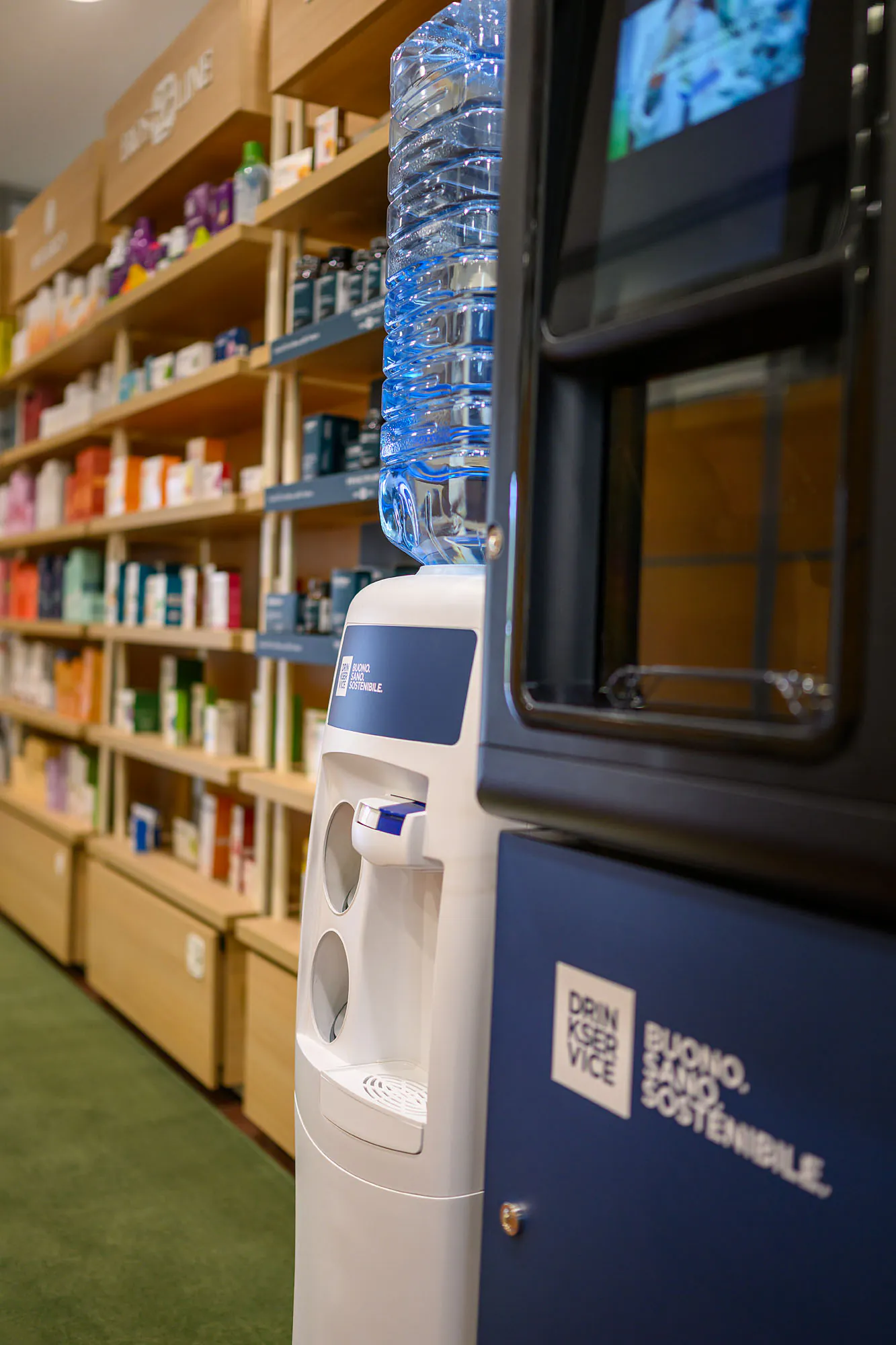 Dispenser con boccione d’acqua accanto al distributore, davanti agli scaffali in legno del punto vendita.