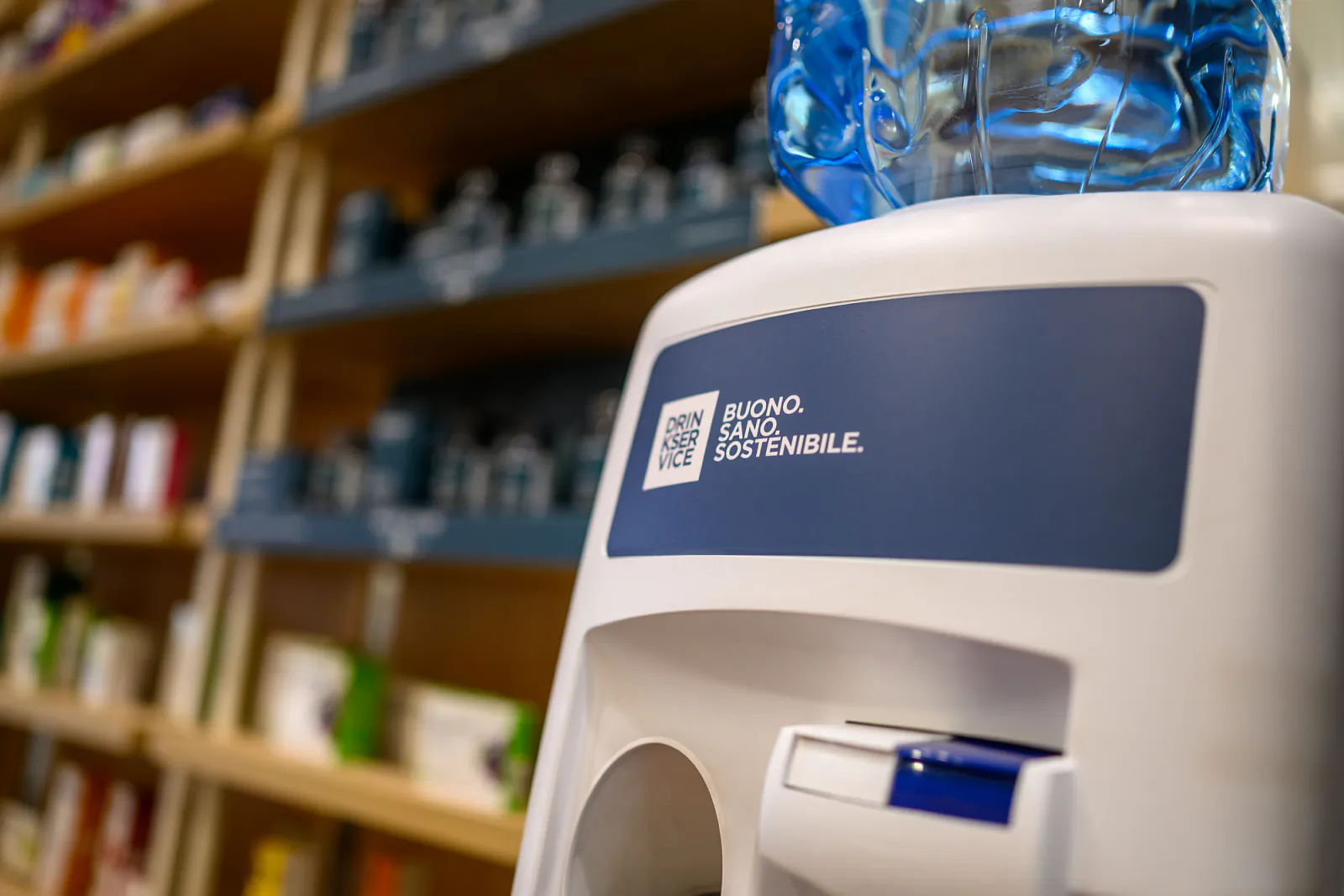 Dispenser con boccione d’acqua accanto al distributore, davanti agli scaffali in legno del punto vendita.
