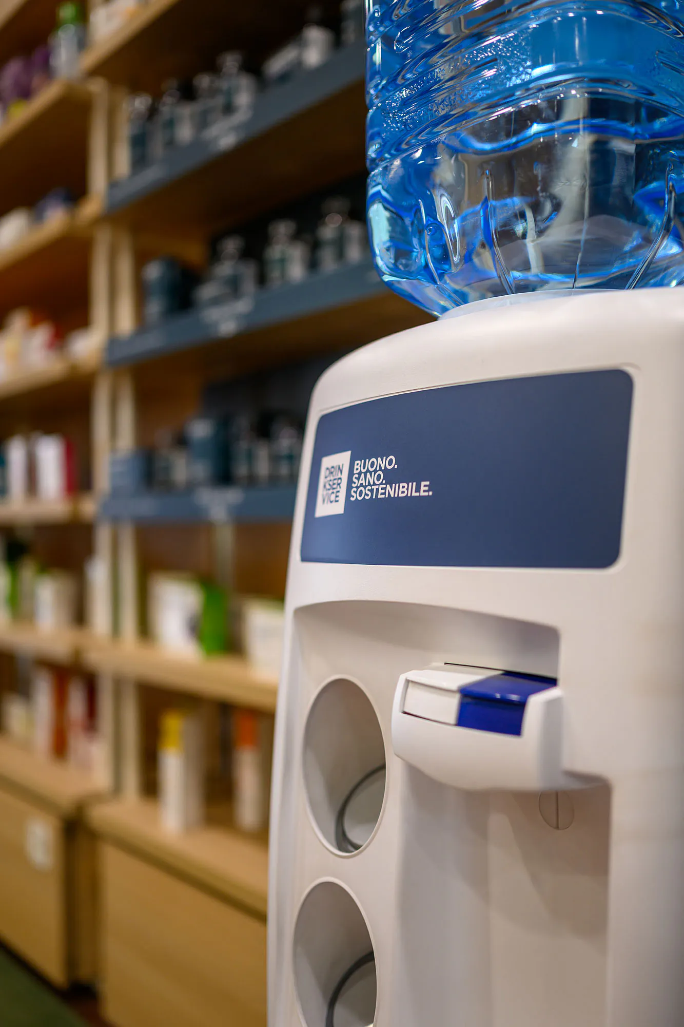 Dispenser con boccione d’acqua accanto al distributore, davanti agli scaffali in legno del punto vendita.