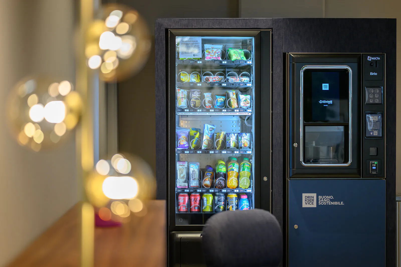 Il distributore di snack fotografato oltre le lampade sferiche dorate, con i riflessi caldi in primo piano.