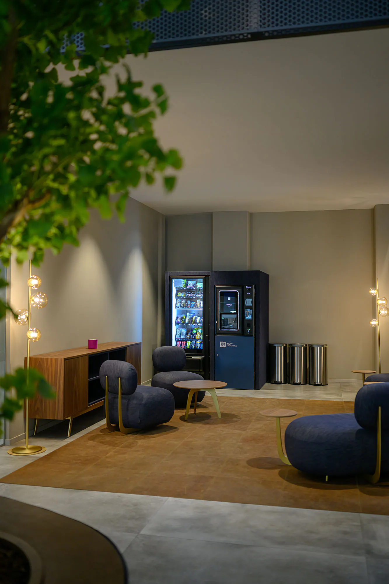 Area break con distributori rivestiti in denim blu, sedute coordinate e illuminazione decorativa.