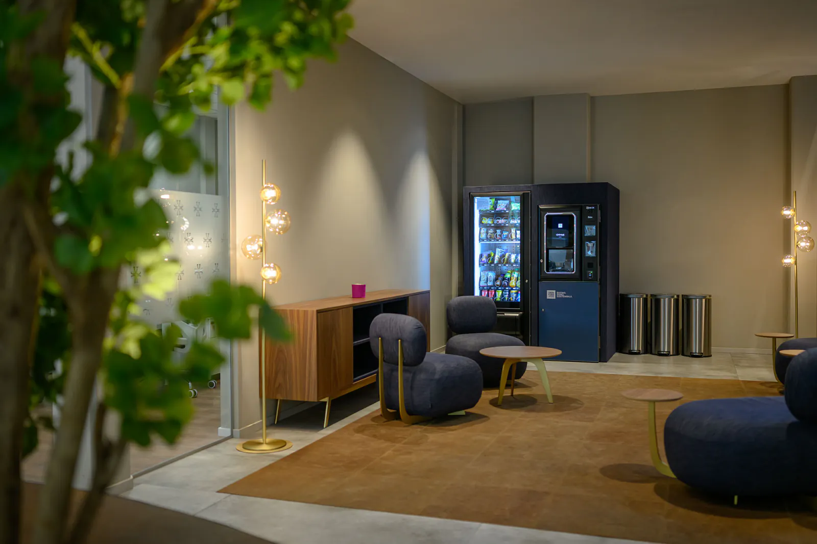 Area break con distributori rivestiti in denim blu, sedute coordinate e illuminazione decorativa.