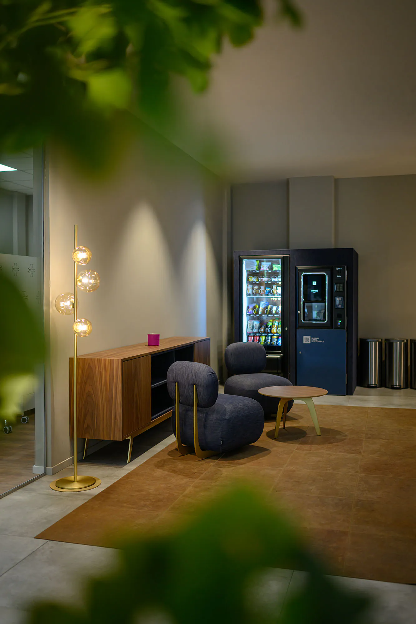 Area break con distributori rivestiti in denim blu, sedute coordinate e illuminazione decorativa.