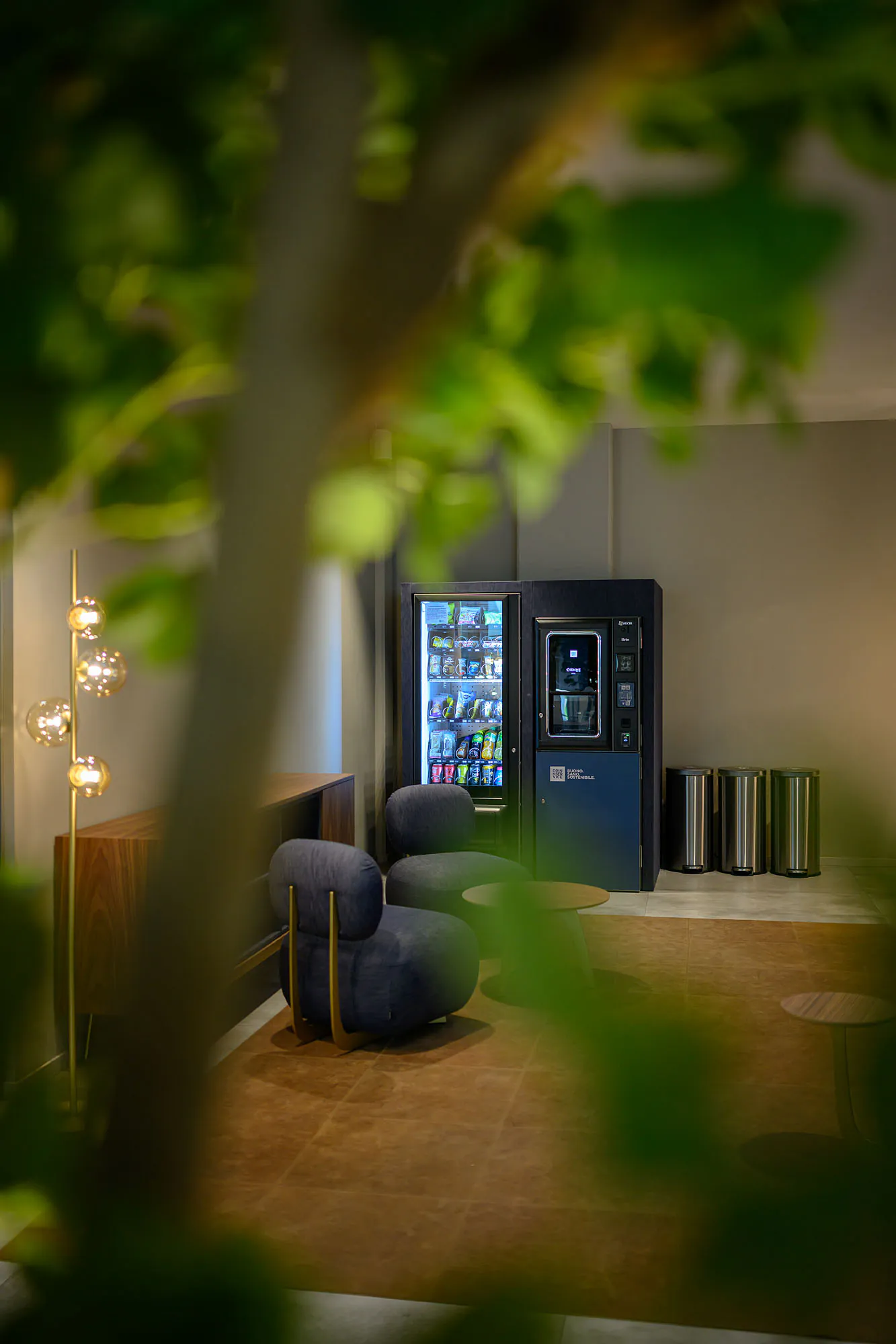 Area break con distributori rivestiti in denim blu, sedute coordinate e illuminazione decorativa.