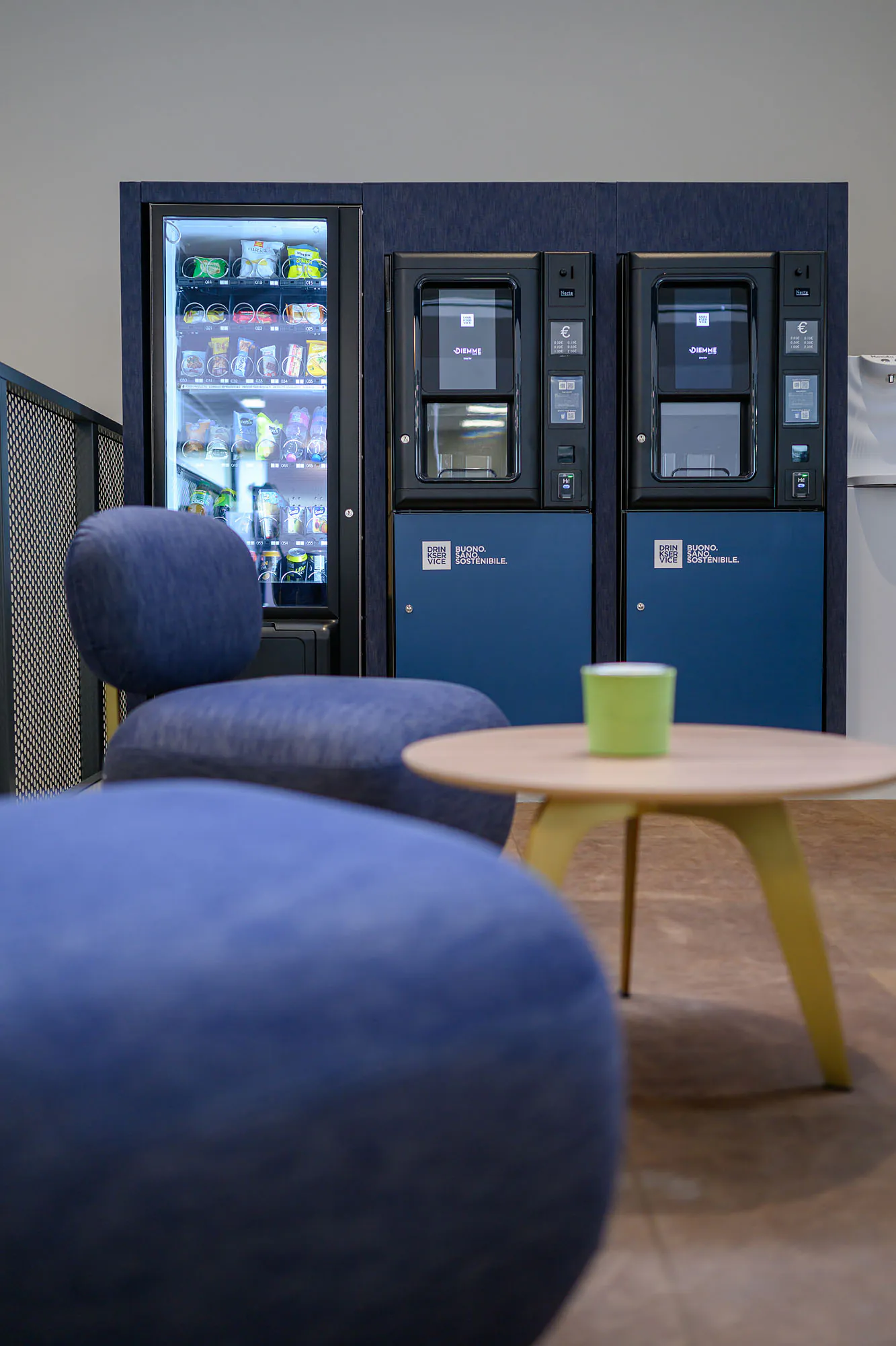 Area break con distributori rivestiti in denim blu, sedute coordinate e illuminazione decorativa.