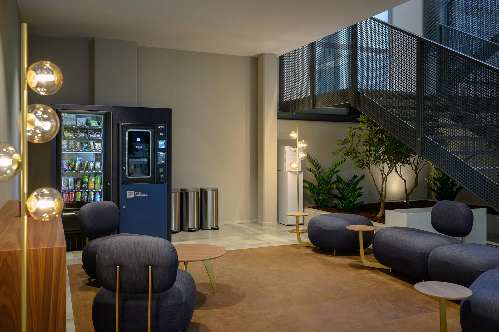 Area break con distributori rivestiti in denim blu, sedute coordinate e illuminazione decorativa.