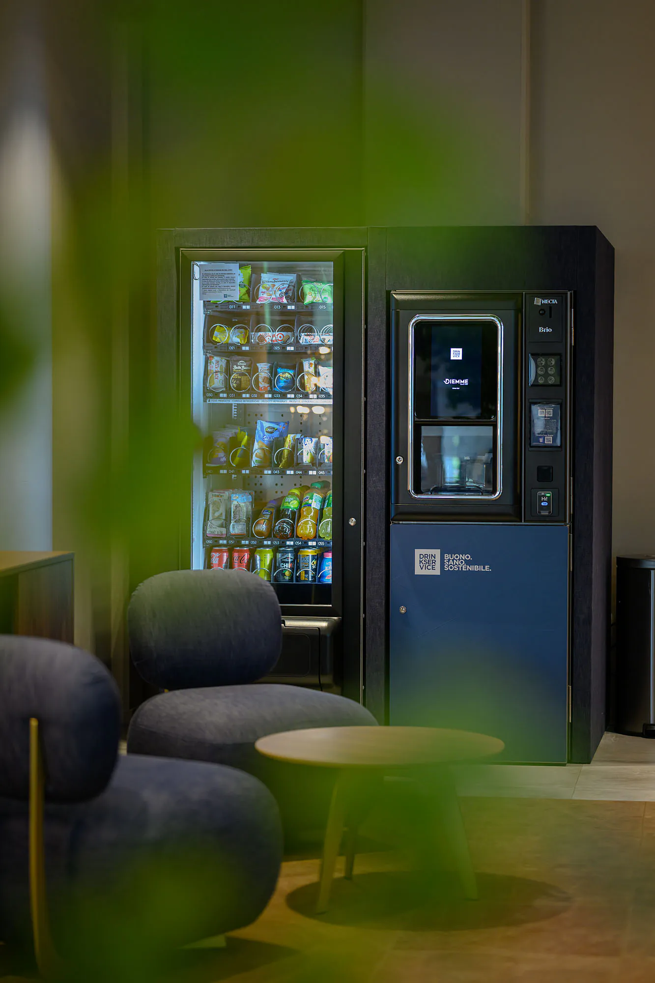 Area break con distributori rivestiti in denim blu, sedute coordinate e illuminazione decorativa.