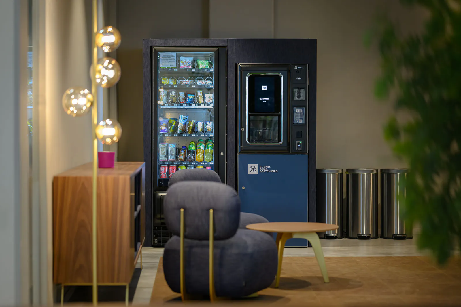 Area break con distributori rivestiti in denim blu, sedute coordinate e illuminazione decorativa.