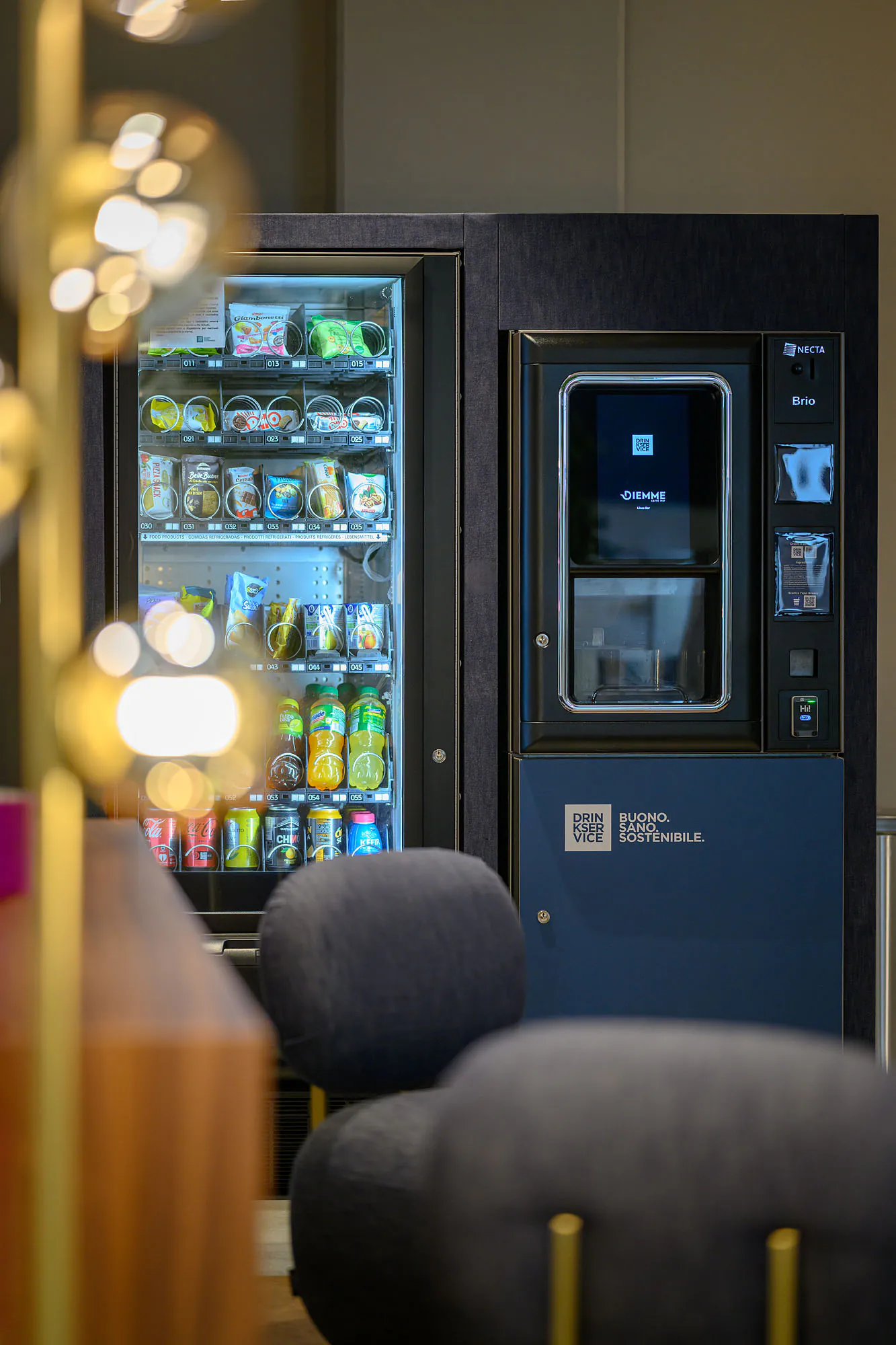 Area break con distributori rivestiti in denim blu, sedute coordinate e illuminazione decorativa.