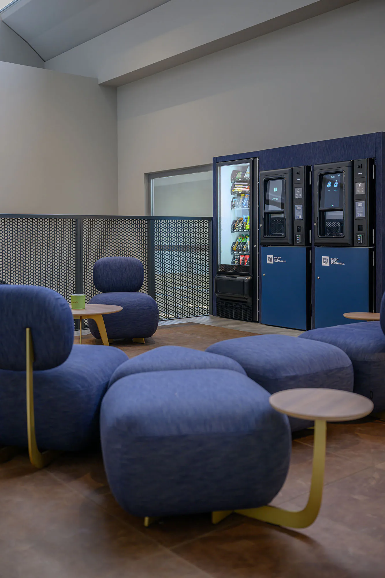 Area break con distributori rivestiti in denim blu, sedute coordinate e illuminazione decorativa.