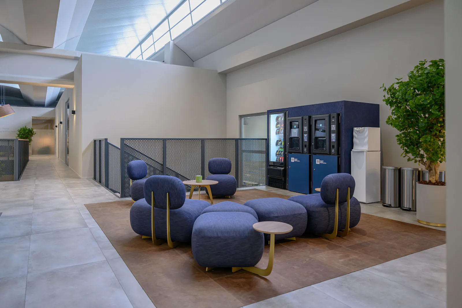 Area break con distributori rivestiti in denim blu, sedute coordinate e illuminazione decorativa.