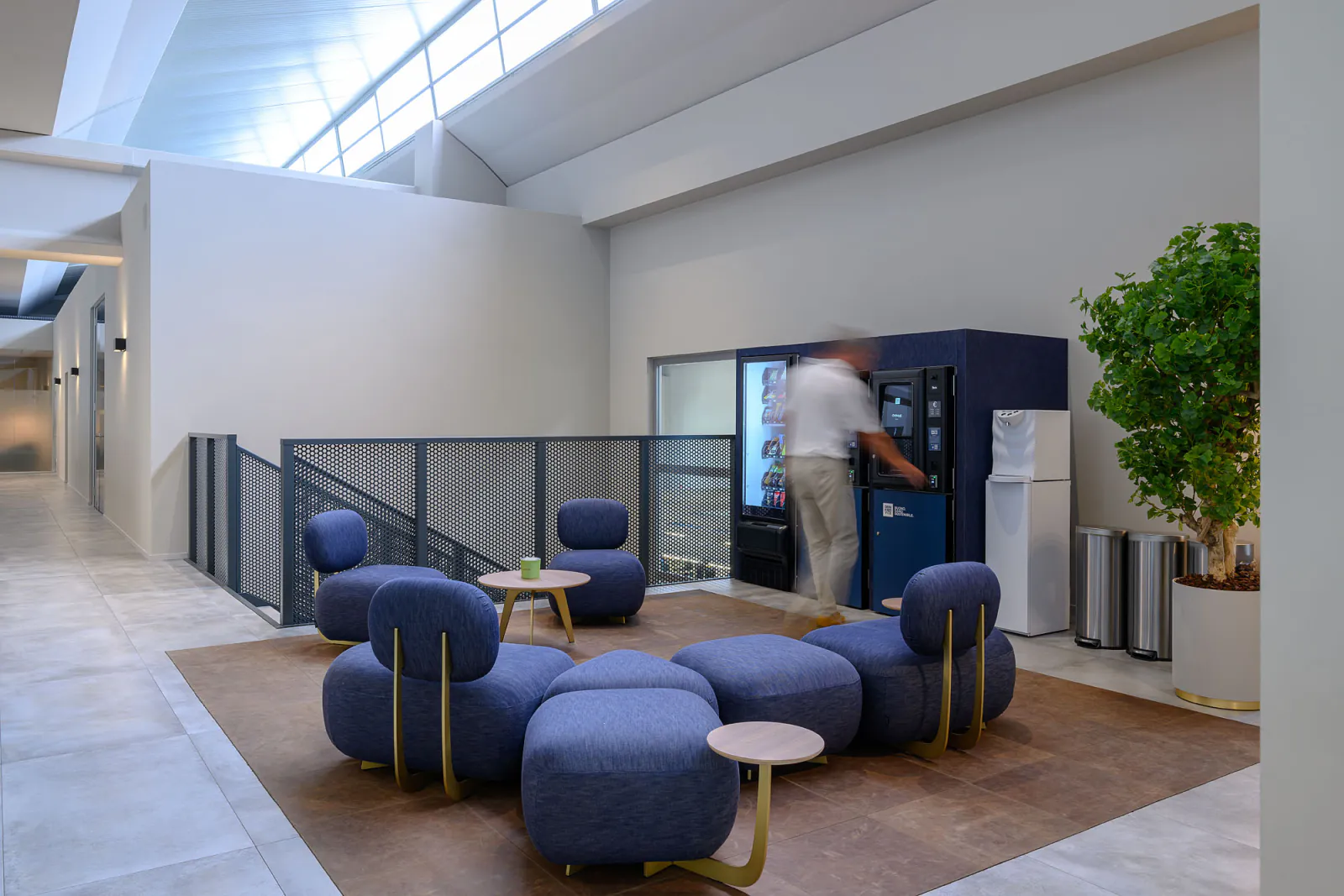 Area break con distributori rivestiti in denim blu, sedute coordinate e illuminazione decorativa.