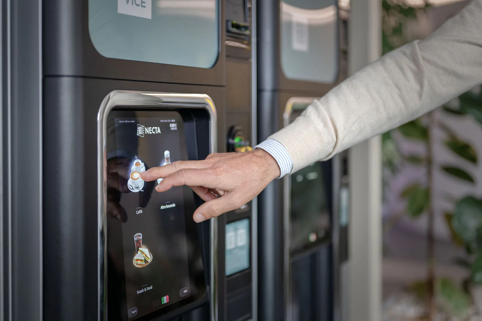 Una mano seleziona una bevanda sul touchscreen di una macchina per il caffe'.