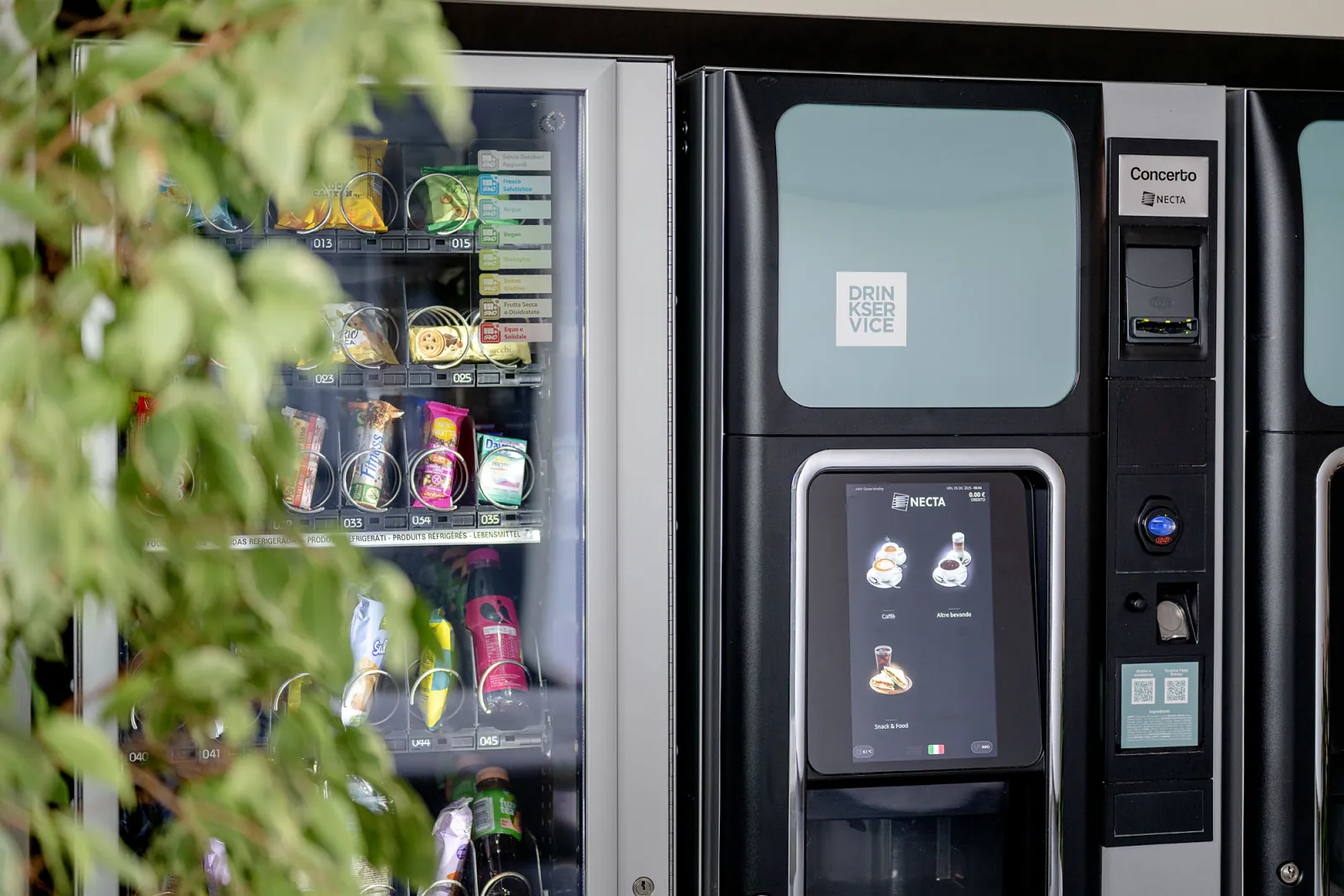 Distributori di bevande, snack e acqua nella hall aziendale, con piante e arredi dell’area ristoro.